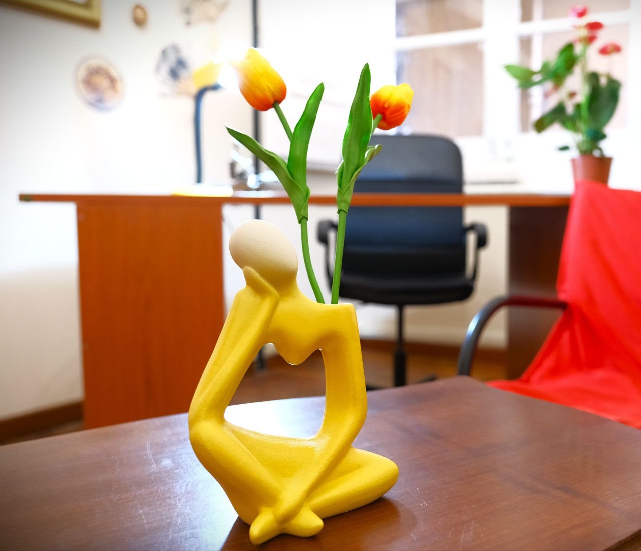 Una piccola scultura gialla a forma di pensatore con dei tulipani
